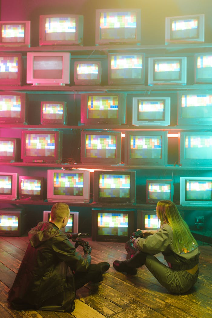 Cyberpunk aesthetic with neon lights and vintage TVs. Two people absorbed in retro tech.